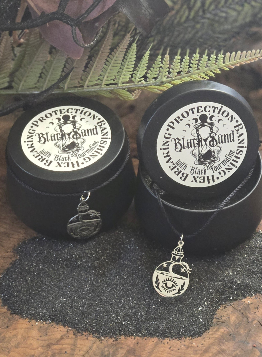 Black sand with ground black tourmaline, infused in a black pot belly cauldron. Tin holder adorned with a spell bottle charm