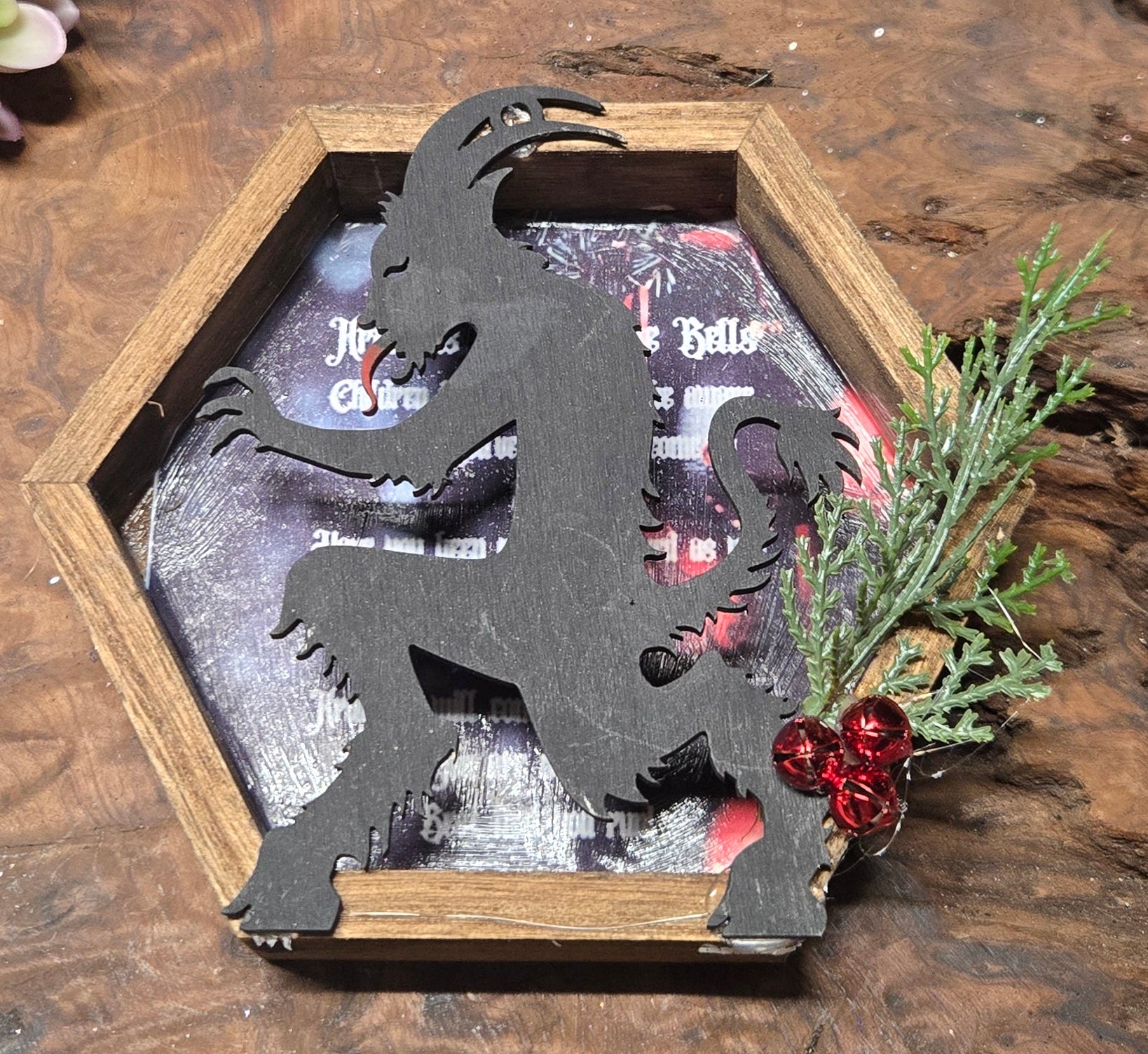 Decorative Krampus silhouette in a wooden frame with festive elements on a wooden surface.