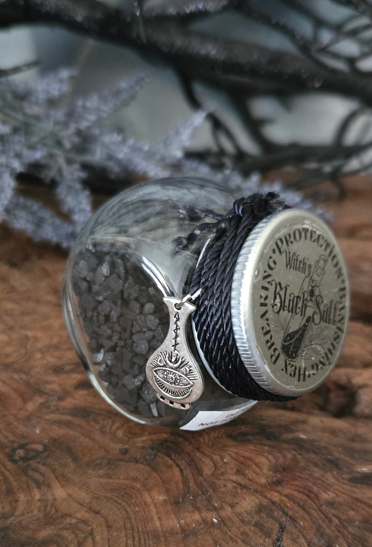 Decorative bottle with black ribbons and a silver pendant on a textured surface. Witchcraft altar supplies — Black Salt in eco-friendly glass jar
