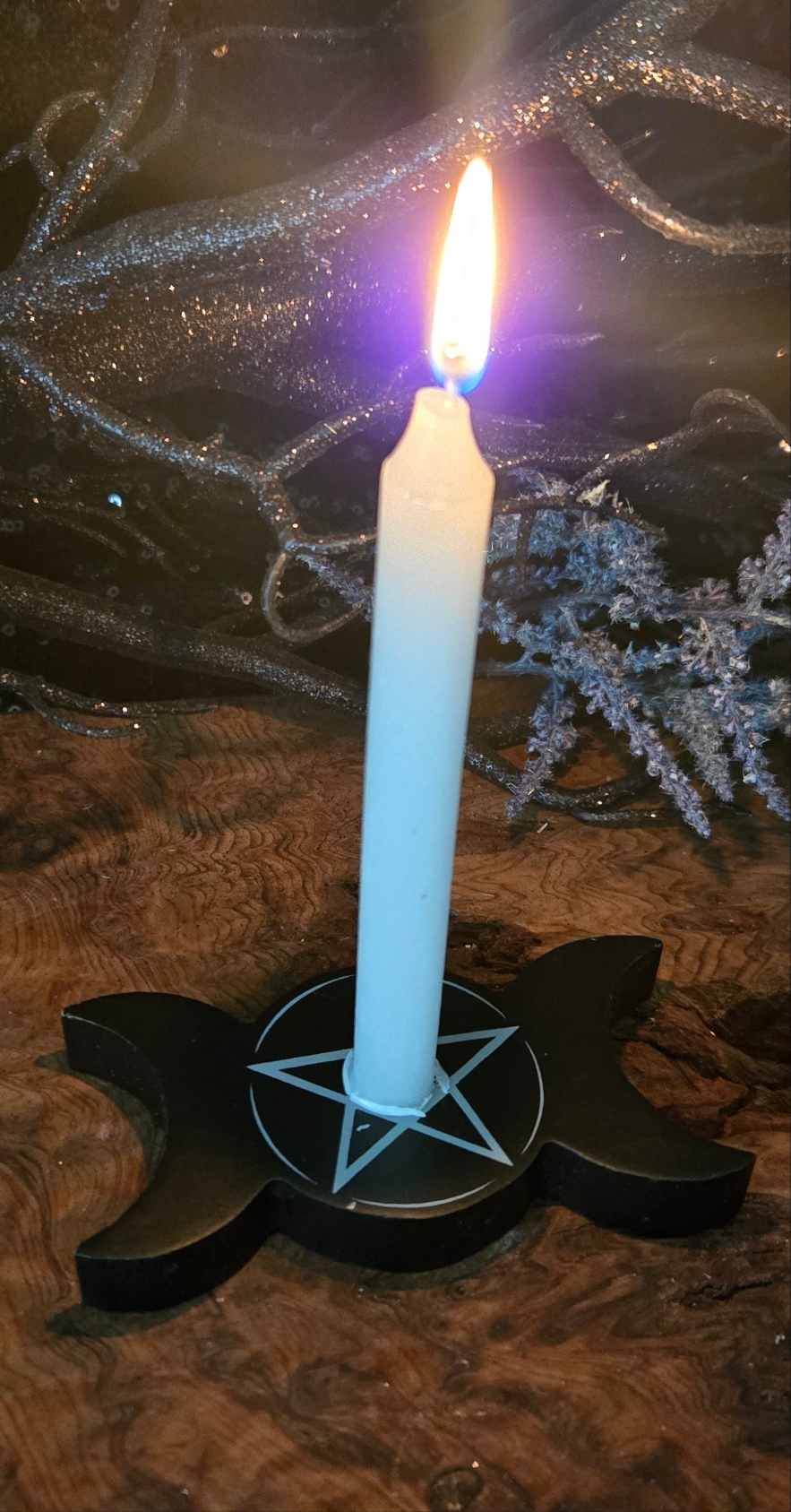 A lit chime candle with a blue flame on a black holder with a pentagram design, surrounded by decorative elements suggesting a magical or ritualistic setting.