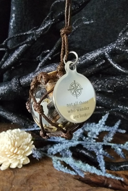 Glass ball held in brown Macrame with spelled herbs and crystals for travel, protection, and not all those who wander are lost. Chrome charm, car charm