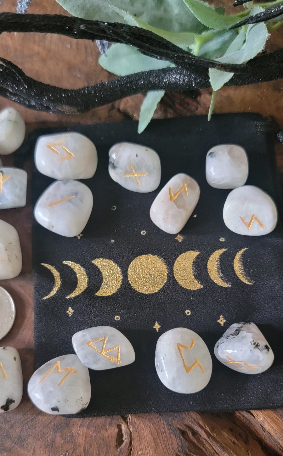 Rainbow moonstone crystal runes with golden symbols and a black velveteen bag with a golden moon phase design