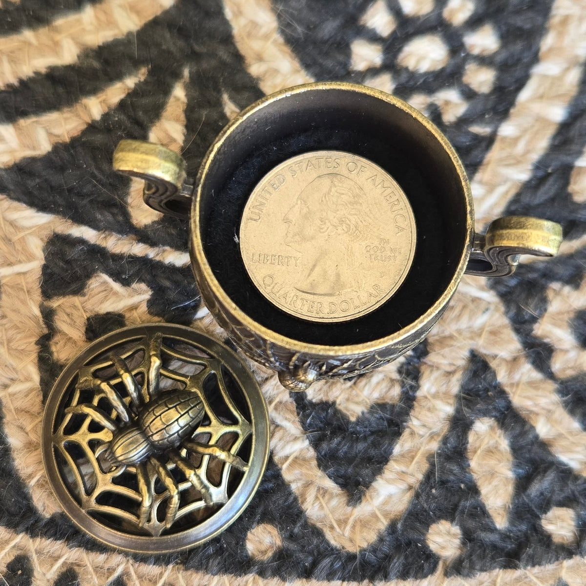 An antique-style metal keepsake box shown open, with a US Quarter coin inside for scale and the spider and web lid placed beside it.