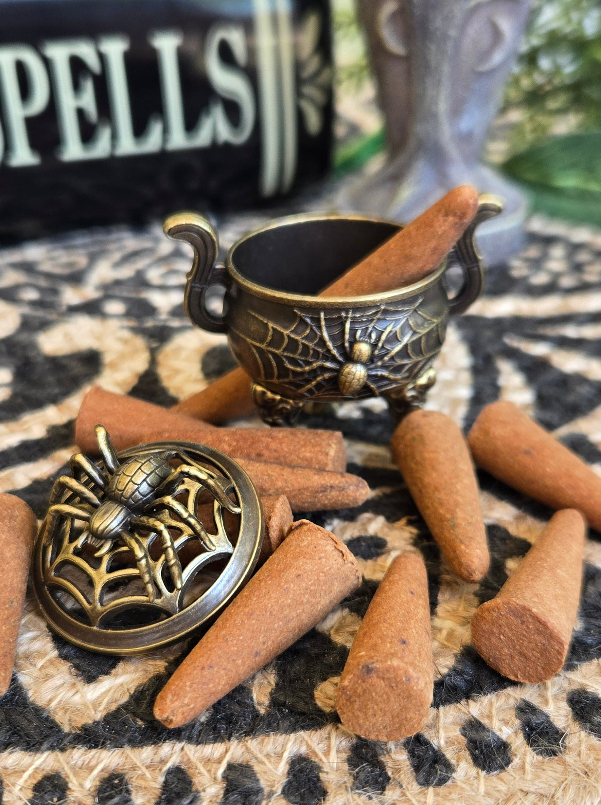 Halloween-themed miniature incense burner featuring a small bronze cauldron, a spiderweb-themed lid, and several brown incense cones for scale.