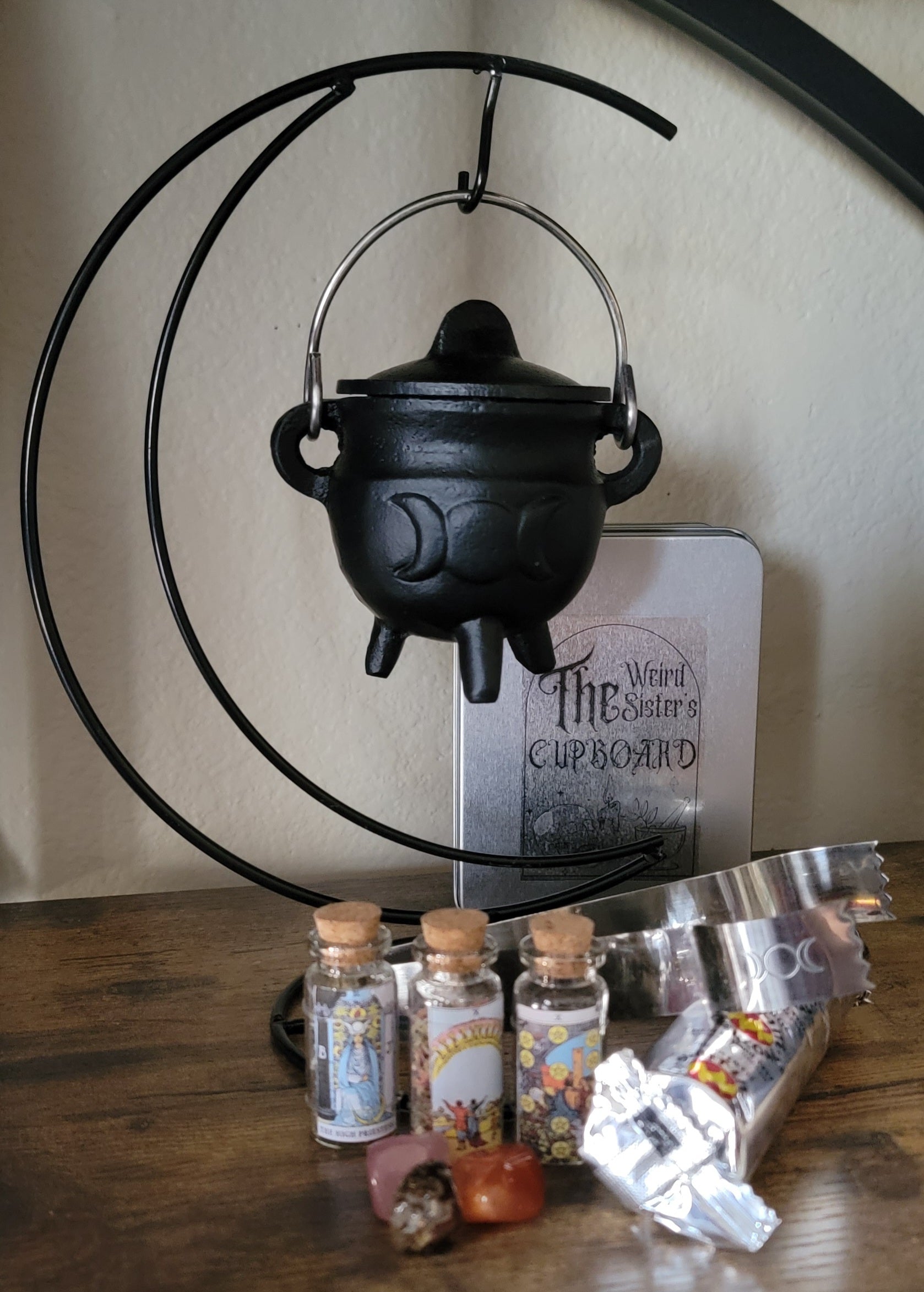 Three inch casr iron cauldron, with the triple moon design being held by a metal Crescent moon, stand with tarot Spell bottle jars, charcoal discs blacksand to complete this bulcket
